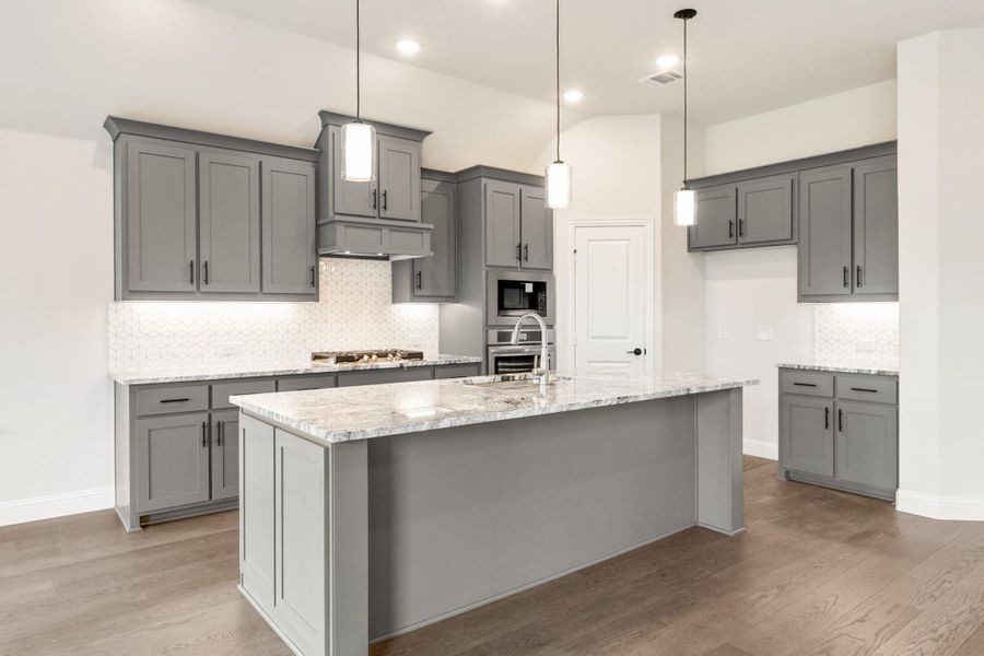 Kitchen with gray cabinets, large island with marble countertops, pendant lights, and hardwood floors Kitchen with gray cabinets, large island with marble countertops, pendant lights, and hardwood floors
