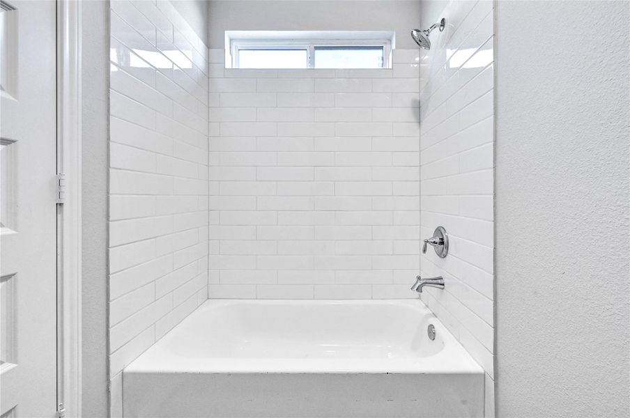 This bathroom features a clean, modern design with a white tiled bathtub and shower combination. It includes chrome fixtures and a small window for natural light.Please note: The image is not the actual home; it is a home with the same floor plan in the neighborhood.