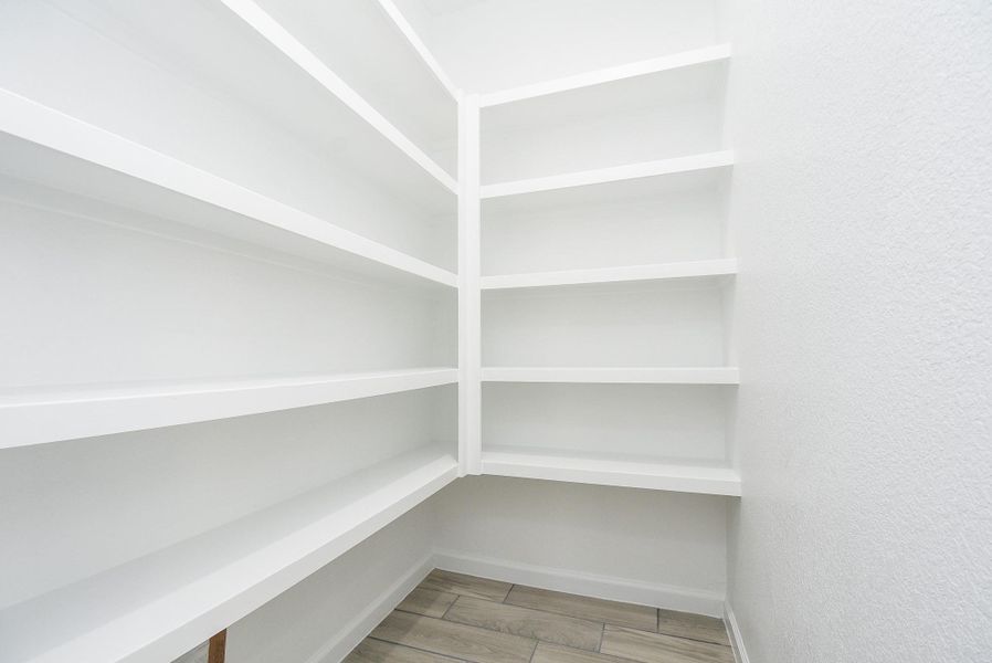 This is a clean, bright, corner walk-in pantry with white shelving and wood-look flooring, offering ample storage space for kitchen essentials. This is a clean, bright, corner walk-in pantry with white shelving and wood-look flooring, offering ample storage space for kitchen essentials.