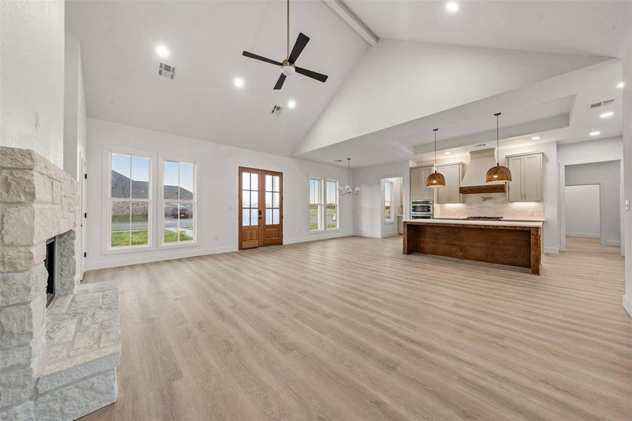 Unfurnished living room with high vaulted ceiling, light wood finished floors, a fireplace, beam ceiling, and a ceiling fan Unfurnished living room with high vaulted ceiling, light wood finished floors, a fireplace, beam ceiling, and a ceiling fan