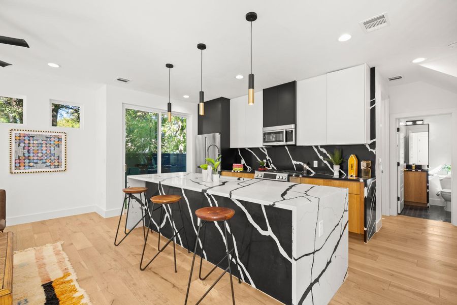 Kitchen featuring a kitchen island with sink, modern cabinets, a kitchen bar, light wood-style flooring, and backsplash Kitchen featuring a kitchen island with sink, modern cabinets, a kitchen bar, light wood-style flooring, and backsplash