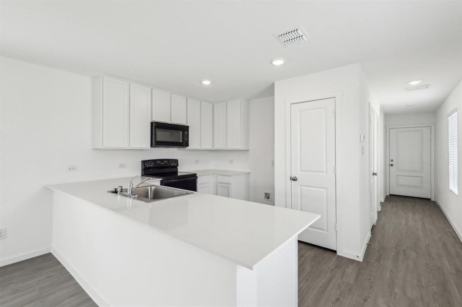 Kitchen featuring white cabinetry, solid surface countertops, black appliances, a stainless steel sink, and wood-finish flooring