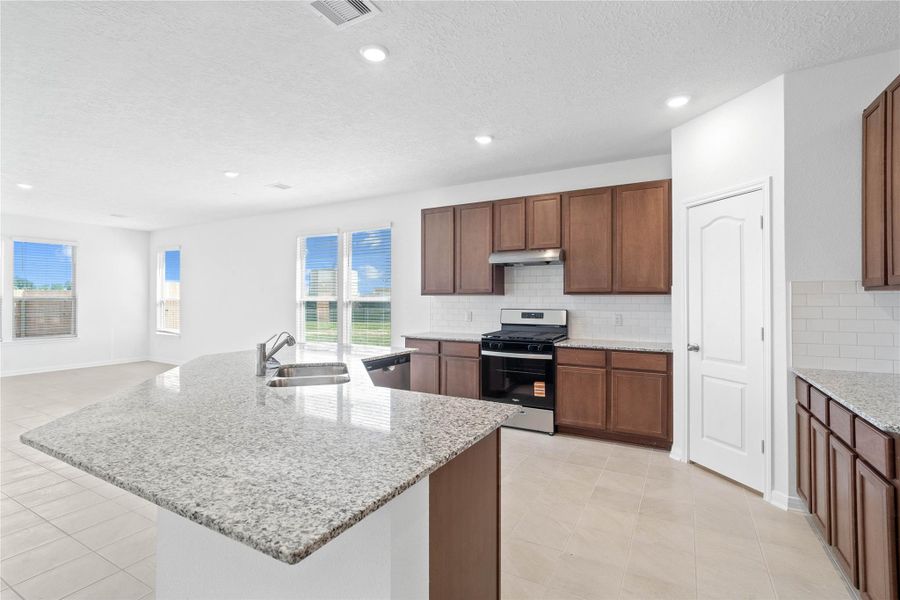 This spacious kitchen boasts soaring ceilings, Woodmont Cody cabinets in a Ginger stain, Granite Luna Pearl countertops, stainless steel Whirlpool appliances, a modern Daltile backsplash, recessed lighting, an extended breakfast bar countertop, and a pantry—all overlooking the expansive family room.