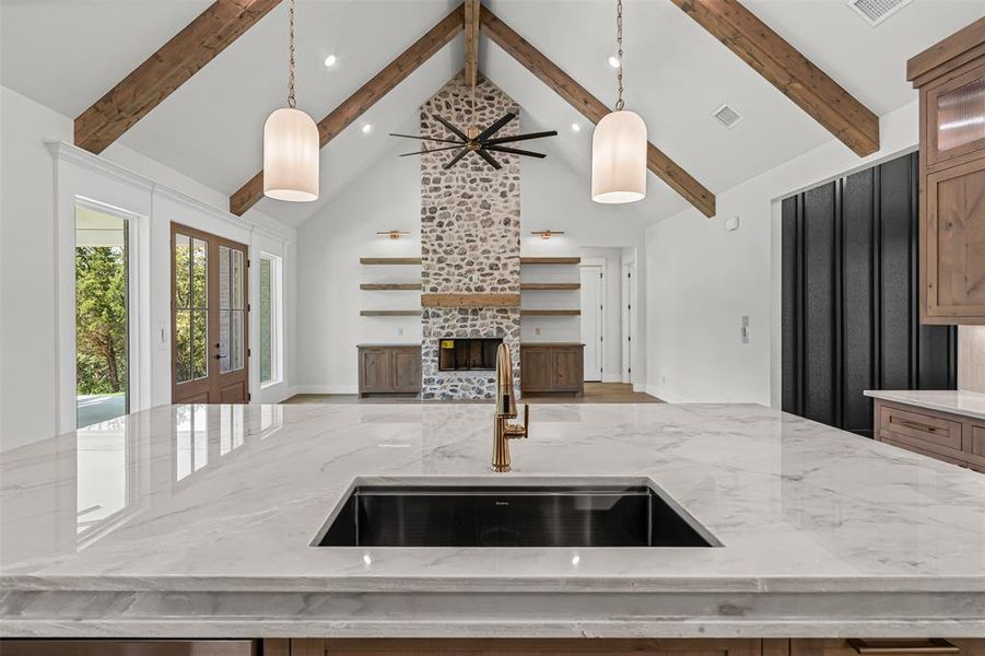 Kitchen featuring high vaulted ceiling, light stone counters, an island with sink, decorative light fixtures, and open floor plan Kitchen featuring high vaulted ceiling, light stone counters, an island with sink, decorative light fixtures, and open floor plan