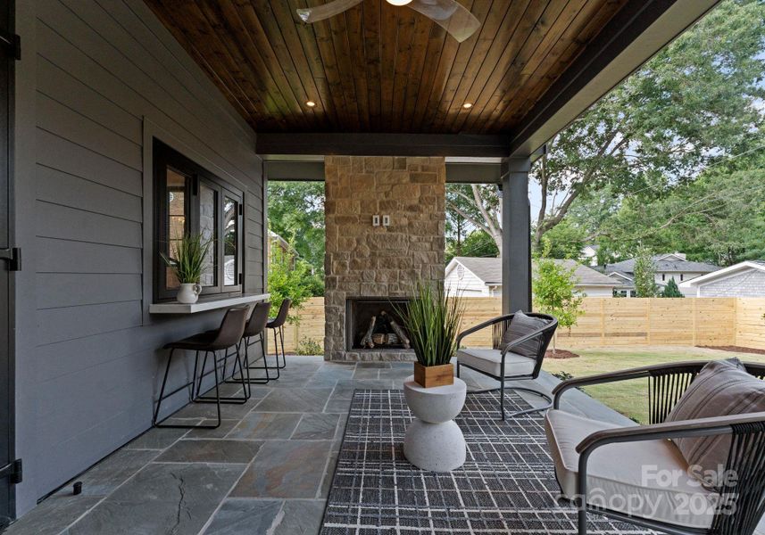 Covered back porch with stone cast fireplace, full color flagstone for porch floors, and surround sound. The back porch also includes sliding accordion kitchen window to back porch with custom quartz bar and seating. Covered back porch with stone cast fireplace, full color flagstone for porch floors, and surround sound. The back porch also includes sliding accordion kitchen window to back porch with custom quartz bar and seating.