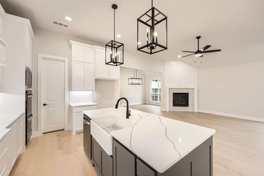 Kitchen featuring white cabinetry, hanging light fixtures, an island with sink, and light hardwood / wood-style flooring