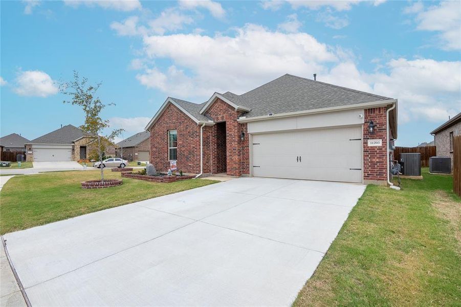 View of front of house with cooling unit, a garage, and a front lawn