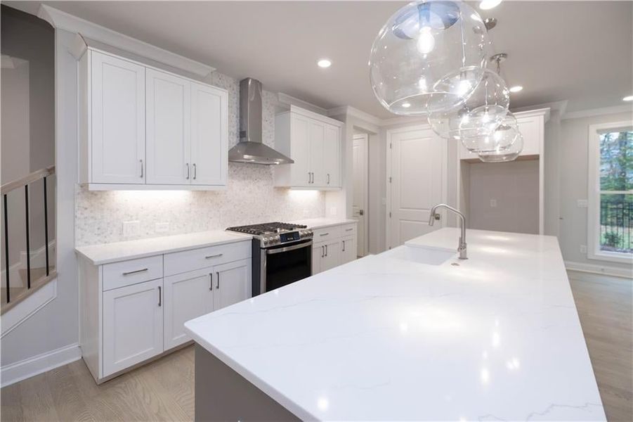 Kitchen featuring white cabinets, hanging light fixtures, light stone counters, gas range, and wall chimney range hood