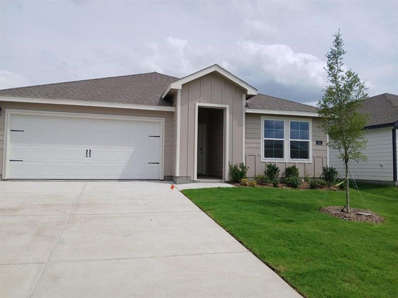 Single-story residence featuring a two-car garage with decorative hardware, a light brown facade, and a dark shingle roof Single-story residence featuring a two-car garage with decorative hardware, a light brown facade, and a dark shingle roof