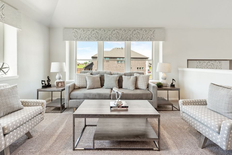 Living room with gray sofa, patterned accent chairs, wood coffee table, and large windows with neighborhood view