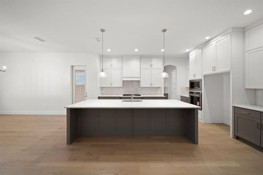 Kitchen featuring white cabinets, arched walkways, hanging light fixtures, light wood-type flooring, and recessed lighting