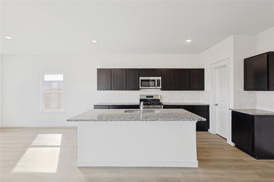 Kitchen featuring light stone counters, a center island with sink, stainless steel appliances, and light hardwood / wood-style floors