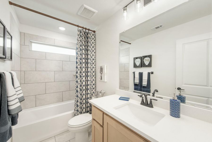 Bathroom with tiled tub and shower, single vanity with white countertop, and large mirror Bathroom with tiled tub and shower, single vanity with white countertop, and large mirror