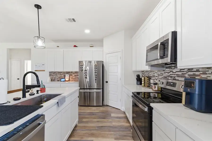 Kitchen with stainless steel appliances, white cabinetry, light wood finished floors, pendant lighting, and light stone counters Kitchen with stainless steel appliances, white cabinetry, light wood finished floors, pendant lighting, and light stone counters