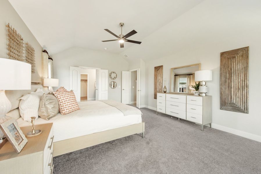 Master bedroom with vaulted ceiling, ceiling fan, gray carpet, and white dresser with mirror