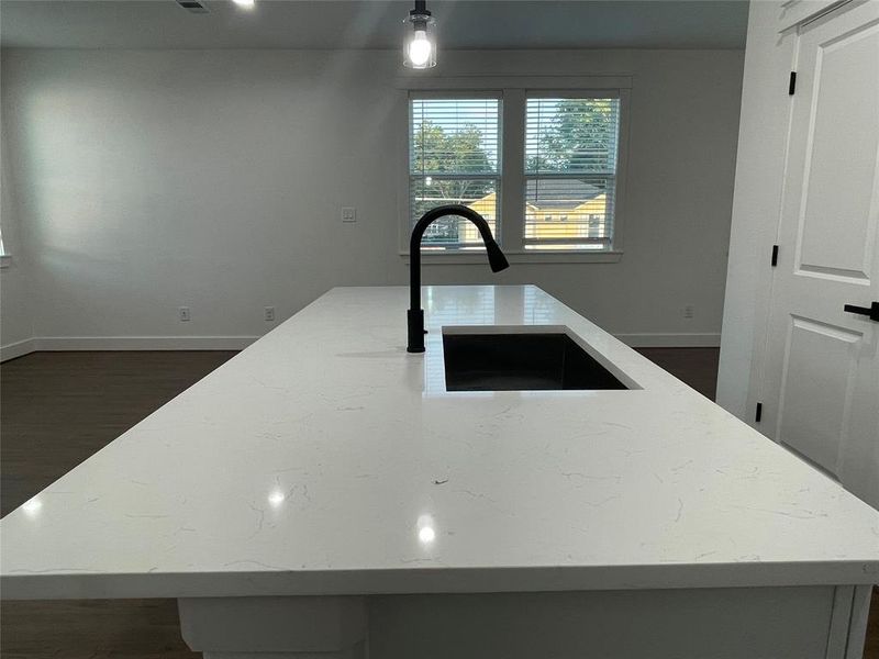 Kitchen with light stone counters, dark wood-style flooring, and an island with sink
