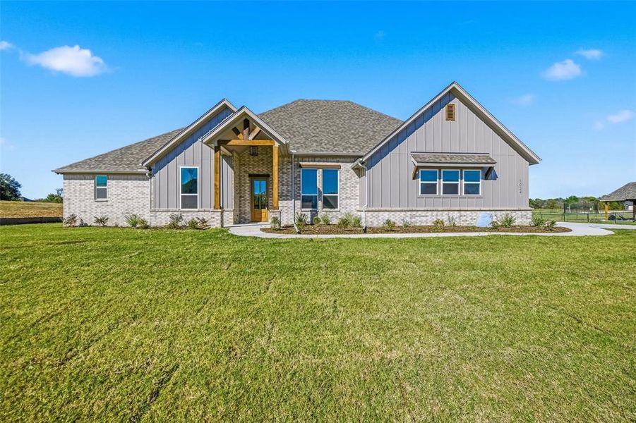 Modern farmhouse featuring board and batten siding, a front yard, and a shingled roof