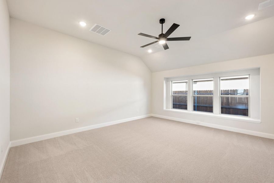 Empty bedroom with vaulted ceiling, ceiling fan, carpet flooring, and triple window