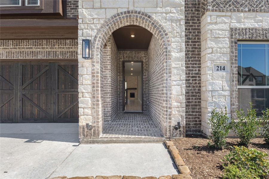 Home entrance with brick arched entryway, dark front door, and wood garage door beside it Home entrance with brick arched entryway, dark front door, and wood garage door beside it
