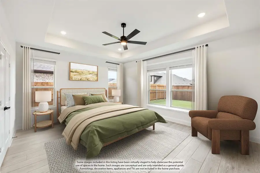 Bedroom with tray ceiling, ceiling fan, light wood floors, and large windows with backyard view