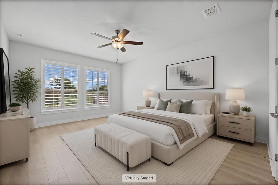 Sun-filled bedroom featuring light wood flooring, plantation shutters, and a ceiling fan for comfort.