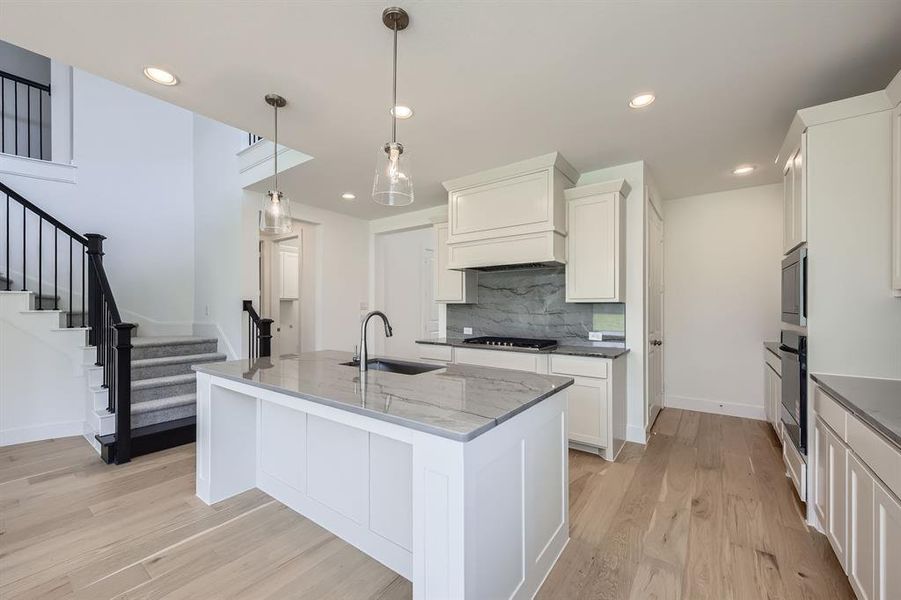 Kitchen featuring a sink, stainless steel appliances, light wood-type flooring, tasteful backsplash, and light stone countertops Kitchen featuring a sink, stainless steel appliances, light wood-type flooring, tasteful backsplash, and light stone countertops