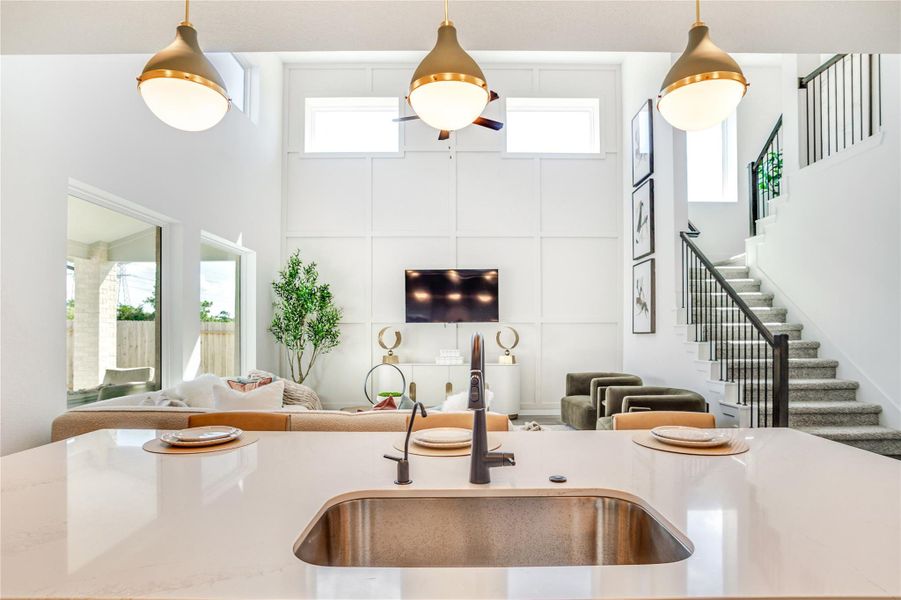 This modern, open-concept living space features high ceilings and abundant natural light, with a sleek kitchen island overlooking a cozy living area. A stylish staircase leads to the upper level, and large windows offer a view of the outdoor patio. This modern, open-concept living space features high ceilings and abundant natural light, with a sleek kitchen island overlooking a cozy living area. A stylish staircase leads to the upper level, and large windows offer a view of the outdoor patio.