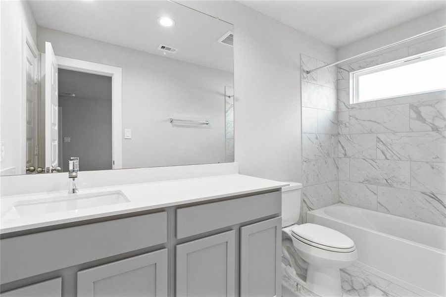 Secondary bath features tile flooring, bath/shower combo with tile surround, stained cabinets, beautiful light countertops, mirror, sleek fixtures and modern finishes.