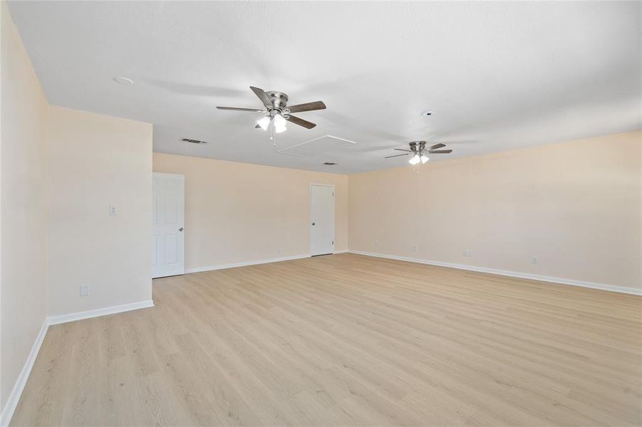 Empty room with a ceiling fan, light wood-type flooring, and attic access