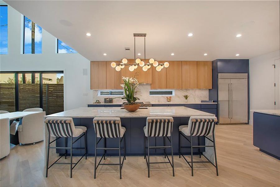 Kitchen featuring a large island with sink, light stone countertops, a breakfast bar, and stainless steel built in refrigerator