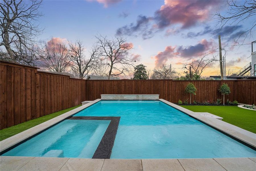 Pool at dusk featuring a fenced backyard, a pool with connected hot tub, and a patio Pool at dusk featuring a fenced backyard, a pool with connected hot tub, and a patio