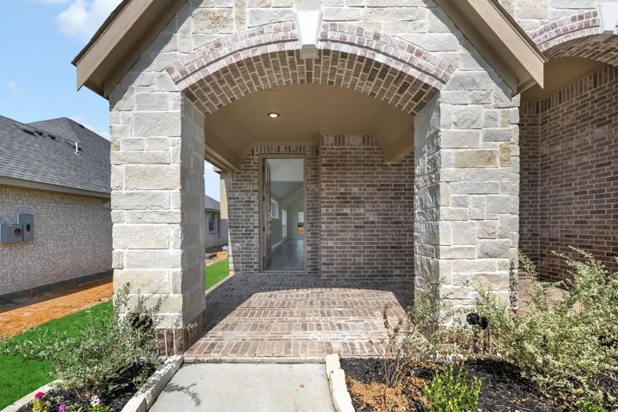 Covered front entry with brick and stone archway, brick porch floor, and front door with view inside