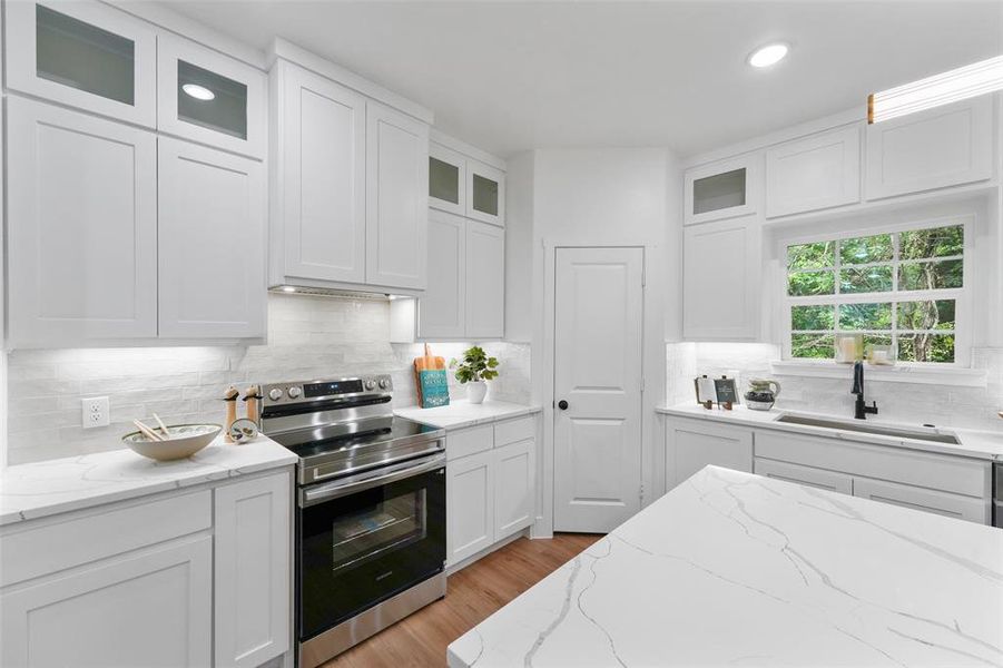Kitchen featuring extensive white cabinetry, light-toned countertops, tile backsplash, stainless steel range, and wood-finish flooring Kitchen featuring extensive white cabinetry, light-toned countertops, tile backsplash, stainless steel range, and wood-finish flooring