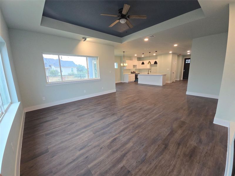 Unfurnished living room with a tray ceiling, ceiling fan, dark wood-style floors, and recessed lighting