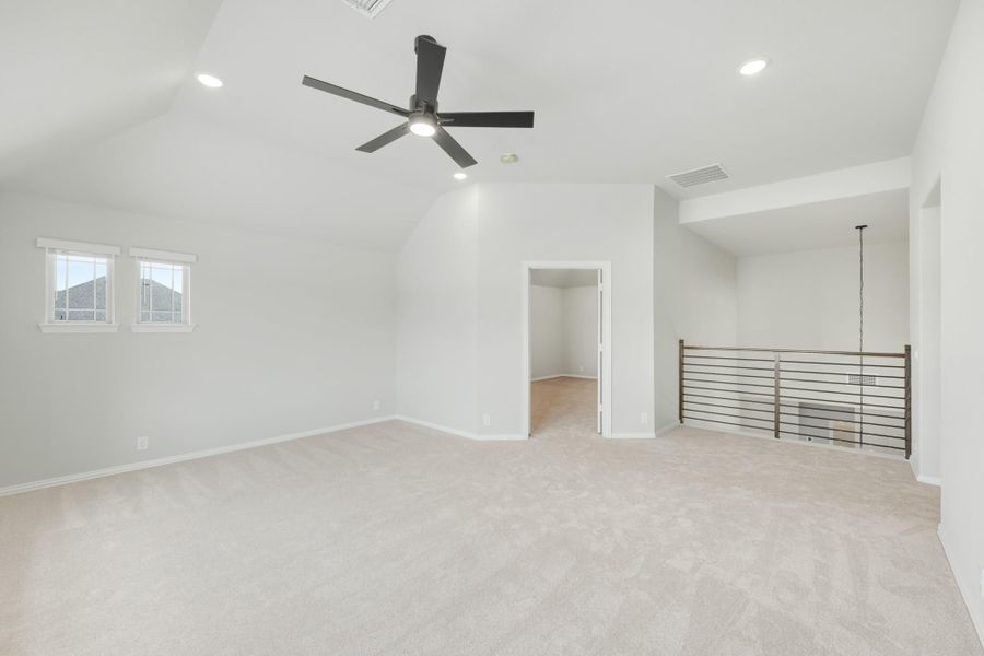 Open upstairs bonus room with vaulted ceiling, ceiling fan, carpet, and metal railing overlooking staircase Open upstairs bonus room with vaulted ceiling, ceiling fan, carpet, and metal railing overlooking staircase