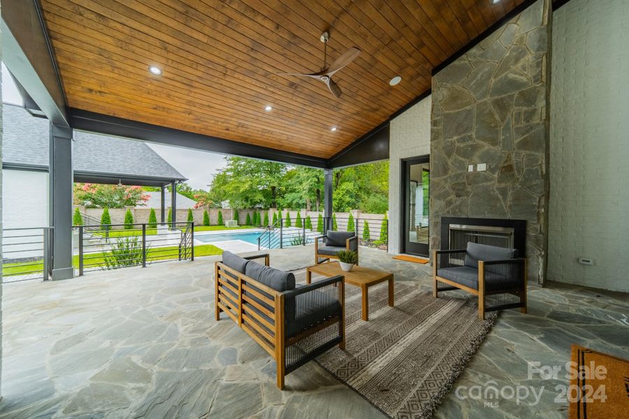 Covered back porch with fireplace, flagstone flooring and view of pool