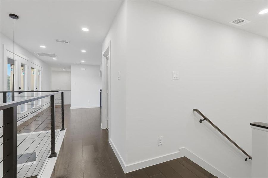 Upper-level hallway featuring dark wood-finish flooring, recessed lighting, white walls, and a contemporary cable railing system