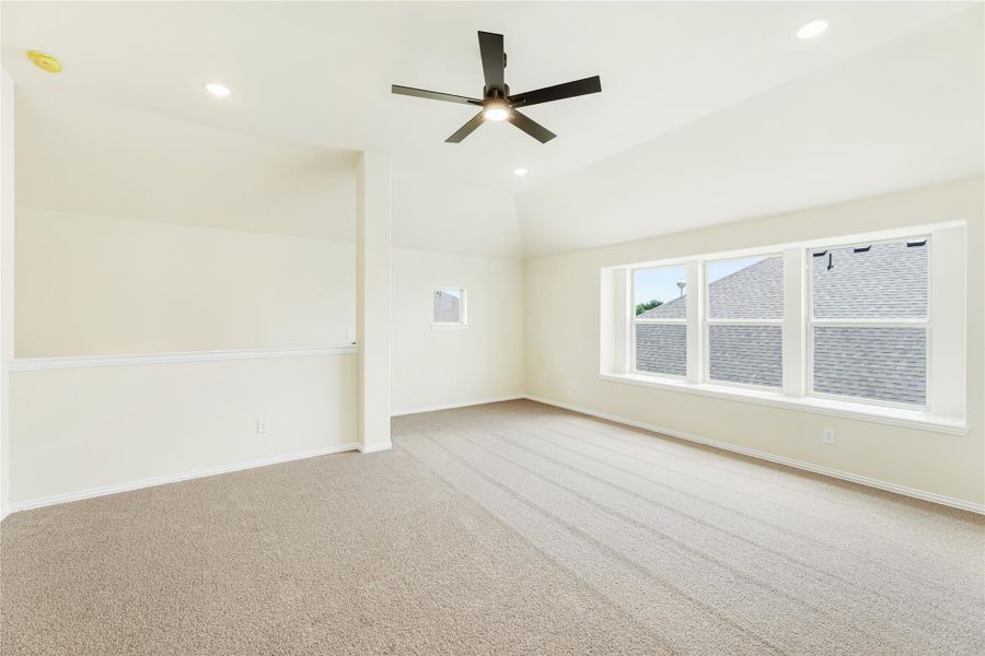 Empty bedroom with vaulted ceiling, ceiling fan, carpet flooring, and large windows along one wall. Empty bedroom with vaulted ceiling, ceiling fan, carpet flooring, and large windows along one wall.