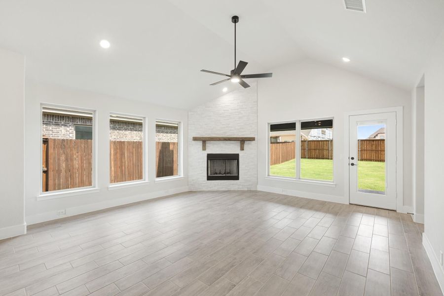 Open living room with vaulted ceiling, white brick fireplace, ceiling fan, and wood-look tile floors