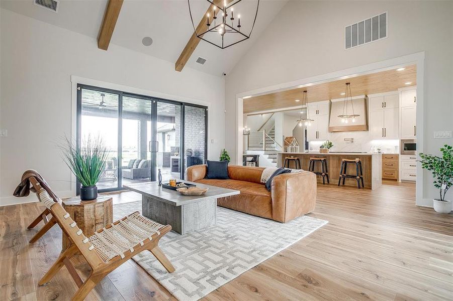 Living area featuring high vaulted ceiling, a chandelier, light wood-type flooring, stairs, and beam ceiling
