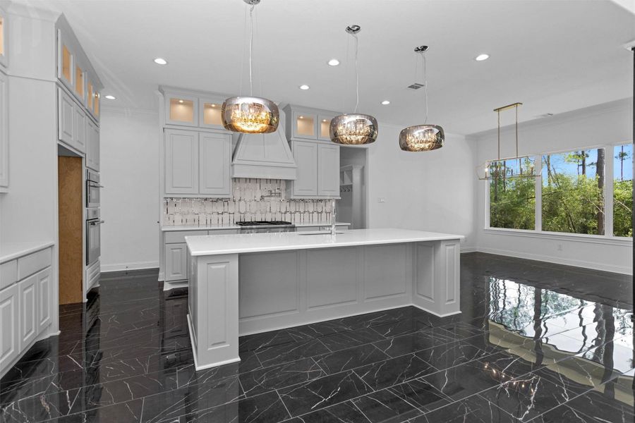 This chef-inspired kitchen is the heart of the home, featuring a grand island, designer tile backsplash, statement lighting, and oversized windows.