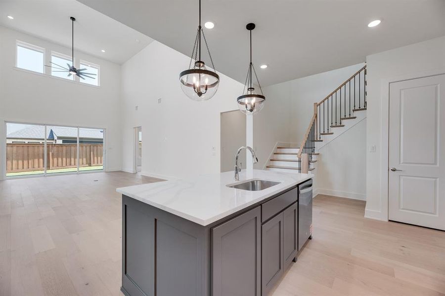 Kitchen featuring light wood-style flooring, pendant lighting, light stone countertops, a kitchen island with sink, and recessed lighting