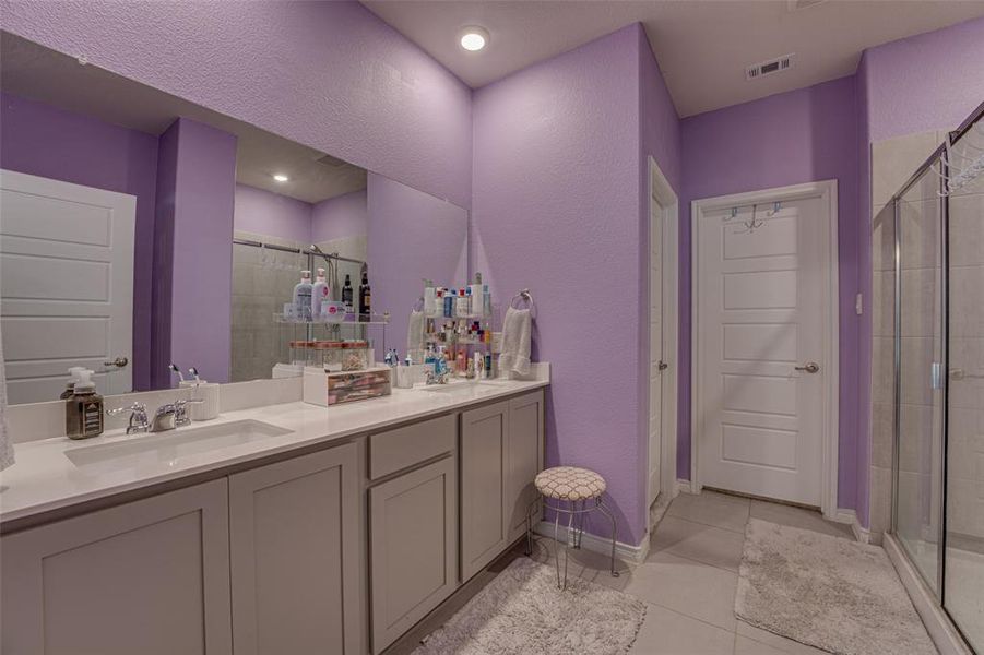 Bathroom with light tile patterned floors, a stall shower, double vanity, and a textured wall