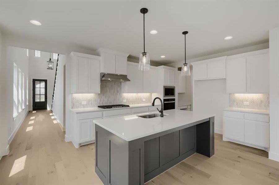 Modern kitchen featuring a large central island with a sink, white cabinetry, a built-in oven, and a gas range