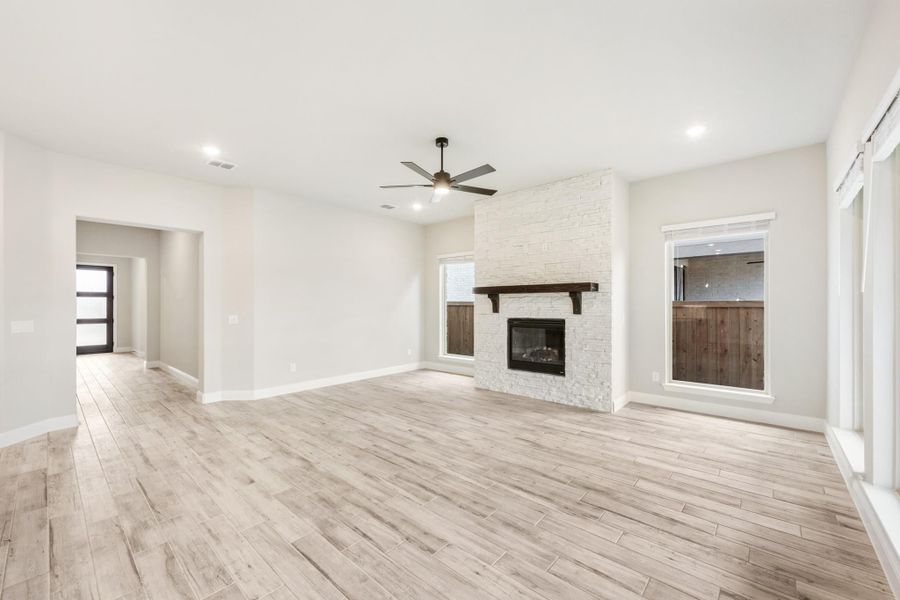 Open living room with light wood floors, white brick fireplace, and ceiling fan