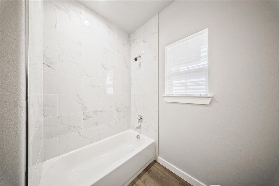 Bathroom featuring shower / tub combination and wood finished floors Bathroom featuring shower / tub combination and wood finished floors