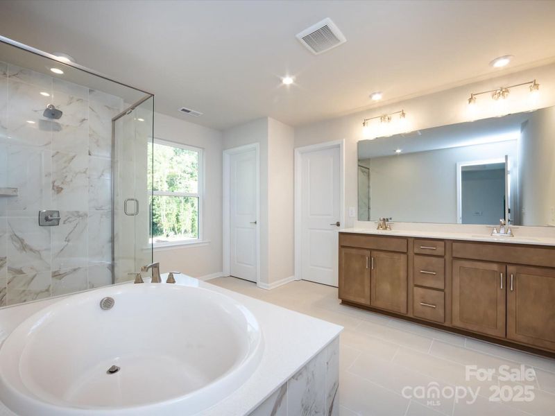 En suite primary bath with modern yet timeless wood-toned cabinetry.
