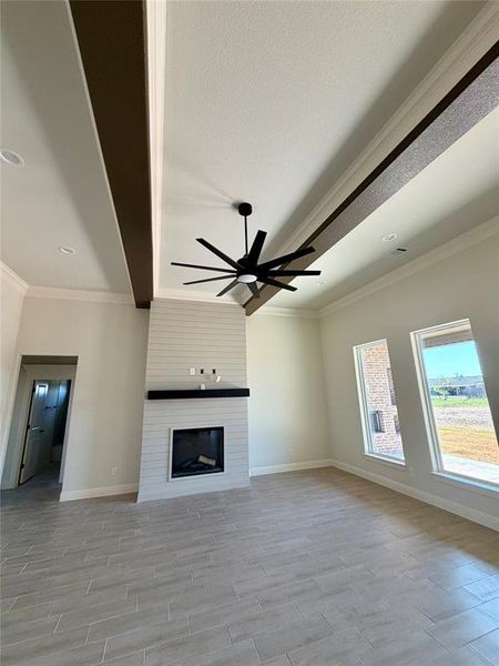 Unfurnished living room featuring crown molding, wood tiled floors, a large fireplace, a ceiling fan, and beamed ceiling Unfurnished living room featuring crown molding, wood tiled floors, a large fireplace, a ceiling fan, and beamed ceiling