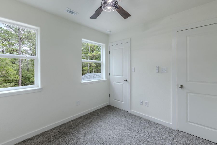 Well-lit sleeping quarters with treetop views through broad windows and a contemporary ceiling fan. Well-lit sleeping quarters with treetop views through broad windows and a contemporary ceiling fan.
