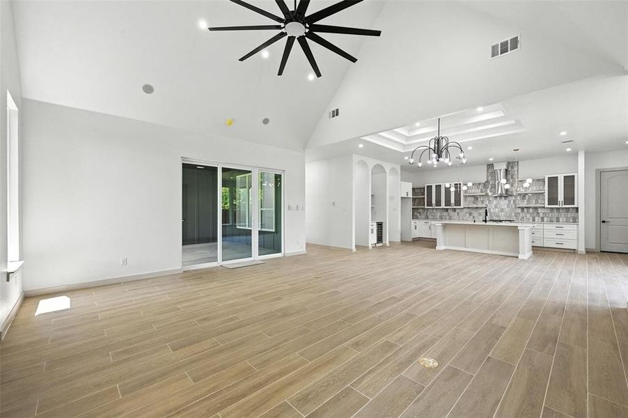 Unfurnished living room with high vaulted ceiling, recessed lighting, light wood-style floors, arched walkways, and a chandelier Unfurnished living room with high vaulted ceiling, recessed lighting, light wood-style floors, arched walkways, and a chandelier